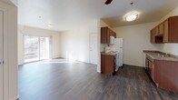 This single-floor residence offers a well-organized layout designed for comfortable everyday living. The open-concept living and dining area is finished with rich, dark wood-style flooring that extends throughout the main spaces, creating a cohesive and inviting atmosphere. A ceiling fan provides added comfort, while a sliding glass door allows natural light to flood the area. The kitchen is efficiently designed in a galley style, featuring warm wood cabinetry, granite-style countertops, a double-basin sink, and white appliances including an electric range, refrigerator, and microwave. The bedroom is carpeted for warmth and comfort, benefits from natural light through a window, and offers generous storage with dual closets. The full bathroom includes dark wood-style flooring that mirrors the main living area, a vanity with granite-style countertops set in rich wood cabinetry, a large mirror, and a full-size tub and shower combination. A dedicated laundry area houses a full-size side-by-side washer and dryer with overhead wire shelving, providing practical in-unit convenience. The overall design is clean and functional, with a neutral color palette throughout.