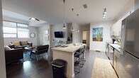 Located at 950 N Tyndall Ave in Tucson, Arizona, this single-floor unit offers a well-designed, contemporary living space with a cohesive modern aesthetic throughout. The open-concept kitchen is a standout feature, equipped with stainless steel appliances, two-tone cabinetry in light wood and white finishes, stone countertops, and a large center island with bar seating illuminated by sleek pendant lighting and track fixtures overhead. Dark hardwood-style flooring flows seamlessly from the kitchen into the expansive living area, which features a ceiling fan, large windows that invite natural light, and an open layout ideal for both relaxing and entertaining. The bedrooms are thoughtfully designed, with at least one offering sweeping views of the surrounding Tucson cityscape and lush greenery through oversized windows. Each bathroom is finished with floor-to-ceiling subway tile, frameless sliding glass shower enclosures, wood-toned cabinetry for storage, and wood-look tile flooring. The unit maintains a clean, neutral palette with white walls throughout, complemented by modern fixtures and finishes that give the space a polished, functional character well-suited to the vibrant Tucson community it calls home.