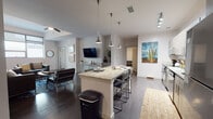 Located at 950 N Tyndall Ave in Tucson, Arizona, this single-floor unit offers a well-designed, contemporary living space with a cohesive modern aesthetic throughout. The open-concept kitchen is a standout feature, equipped with stainless steel appliances, two-tone cabinetry in light wood and white finishes, stone countertops, and a large center island with bar seating illuminated by sleek pendant lighting and track fixtures overhead. Dark hardwood-style flooring flows seamlessly from the kitchen into the expansive living area, which features a ceiling fan, large windows that invite natural light, and an open layout ideal for both relaxing and entertaining. The bedrooms are thoughtfully designed, with at least one offering sweeping views of the surrounding Tucson cityscape and lush greenery through oversized windows. Each bathroom is finished with floor-to-ceiling subway tile, frameless sliding glass shower enclosures, wood-toned cabinetry for storage, and wood-look tile flooring. The unit maintains a clean, neutral palette with white walls throughout, complemented by modern fixtures and finishes that give the space a polished, functional character well-suited to the vibrant Tucson community it calls home.