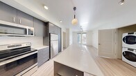 Located at 23040 Military Rd in Kent, WA, this 2-bedroom, 2-bathroom unit offers a well-designed open-concept layout with modern finishes throughout. The kitchen serves as the heart of the home, featuring sleek gray cabinetry, a white quartz countertop island with pendant lighting, stainless steel appliances including a refrigerator, range, and microwave, and a white tile backsplash. Light wood-style flooring flows through the kitchen and living areas, creating a cohesive and contemporary feel. The open living space extends toward a sliding glass door that invites natural light and provides access to a balcony with exterior views. Both bedrooms are carpeted for comfort and feature large windows that bring in ample daylight and views of the surrounding community. Ceiling fans are installed in the main living and bedroom areas. The primary bedroom offers a generous layout with access to a dedicated hallway leading to a closet and bathroom. Both bathrooms are finished with light wood-style flooring, dark vanity cabinetry, white quartz countertops, large mirrors, and full tub-shower combinations. The unit also includes a hallway and closet for added storage, rounding out a practical and polished living space.