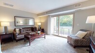 The Maple floor plan is a single-level, two-bedroom, one-bathroom residence thoughtfully designed for comfortable everyday living. The spacious living room serves as the heart of the home, featuring plush wall-to-wall carpeting, neutral gray walls, and a large sliding glass door that opens to a private balcony overlooking lush, tree-lined greenery—flooding the room with natural light. A dedicated dining area sits adjacent to the living space, providing a defined area for meals and entertaining.

The kitchen is efficiently laid out with warm wood-toned cabinetry, light countertops, tile flooring, and white appliances including a gas range, dishwasher, and refrigerator, offering ample storage and functionality.

Both bedrooms are carpeted and well-proportioned, each benefiting from natural light through generously sized windows. Closets with wire shelving systems provide practical storage solutions. The full bathroom features tile flooring, a tub-shower combination, and a wood-toned vanity. Throughout the residence, a cohesive neutral color palette and consistent finishes create a calm, welcoming ambiance.