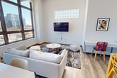 Located on the 5th floor at 212 S 4th Ave in the heart of Ann Arbor, this 750-square-foot apartment offers a thoughtfully designed 2-bedroom, 2-bathroom layout with a contemporary aesthetic throughout. The open-concept living and dining area features light wood flooring, soaring ceilings, and large floor-to-ceiling windows that flood the space with natural light and frame sweeping views of the Ann Arbor skyline. A wall-mounted TV and dedicated workspace add functional versatility to the living area. The kitchen is outfitted with stainless steel appliances, including a gas range, microwave, dishwasher, and refrigerator, complemented by white cabinetry and clean countertops. Both bathrooms feature marble-style tile flooring and walls, with one offering a tub-shower combo behind a sliding glass door and the other a floating vanity with a backlit mirror. The primary bedroom spans 120 square feet and is distinguished by a bold cobalt blue accent wall, a glass-block clerestory window, and a built-in closet. The second bedroom includes an open closet with city-facing windows. Vibrant pops of color throughout the unit give the space an artistic, energetic character.