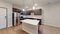 This single-floor residence offers a thoughtfully designed open-concept layout that seamlessly connects the kitchen, dining, and living areas. The kitchen is a standout feature, showcasing dark espresso-toned cabinetry with sleek bar-pull hardware, bright white quartz countertops, and a full suite of stainless steel appliances, including a range, microwave, refrigerator, and dishwasher. A central island with pendant lighting above provides additional workspace and serves as a natural gathering point. Wood-look flooring runs throughout the kitchen and transitions into plush carpeting in the living and sleeping areas.

The living area is open and airy, benefiting from natural light through a sliding glass door fitted with vertical blinds. The bedrooms are generously sized, each featuring soft carpeting, ceiling fans with integrated lighting, and windows with blinds for privacy and light control.

The bathroom is clean and functional, featuring wood-look tile flooring, a dark vanity with a white countertop and single sink, a large mirror, and a full tub-shower combination with chrome fixtures. Neutral tones throughout the space create a cohesive and modern aesthetic well-suited for comfortable everyday living.