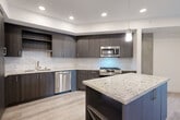 This well-designed one-bedroom, one-bathroom unit offers a thoughtfully arranged single-level floor plan that maximizes every square foot. Light-toned hardwood-style flooring runs throughout the main living areas, creating a cohesive and airy feel.

The contemporary kitchen is a standout feature, showcasing dark espresso cabinetry, granite countertops, and a classic white subway tile backsplash. A central island provides additional prep space and built-in open shelving. Stainless steel appliances — including a gas range, built-in microwave, dishwasher, and a side-by-side refrigerator with ice and water dispenser — complete this functional and stylish space. Recessed lighting and a pendant fixture illuminate the kitchen with ease.

The open living area flows naturally from the kitchen and benefits from a ceiling fan and clean white walls. The bedroom receives natural light through a window with exterior views, and features exposed concrete architectural accents that add an industrial touch.

The walk-in closet offers multi-level shelving and rod systems for organized storage. The bathroom is finished with large-format tile flooring, dark wood cabinetry with a white quartz countertop, a framed mirror, and a glass-enclosed shower with full tile surround. The layout also includes a dedicated hallway connecting the private spaces efficiently.