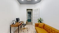 Located at 1900 Westview Blvd in Conroe, Texas, this well-appointed professional space offers a compact yet functional layout across a single floor. The space comprises a private office, a dining/conference room, and a connecting hallway, all designed with a cohesive and polished aesthetic.

The private office is a standout space, featuring crisp white walls accented by a bold slate-gray ceiling with crown molding that adds architectural character. Light wood-style flooring runs throughout, lending warmth and continuity. A rustic wood desk with gold-accented chairs sits alongside a tufted mustard-yellow sofa, creating an inviting yet productive atmosphere. Lush greenery adds a refreshing natural touch, while a classic French door with glass panes provides both privacy and openness.

The conference/dining room exudes sophistication with its dramatic dark ceiling, elegant sputnik chandelier, and wall sconces flanking a striking piece of artwork. A sleek white conference table surrounded by dark upholstered chairs serves as the room's centerpiece. A dark tile fireplace anchors one wall, while patterned drapery frames a window that brings in natural light. A wall-mounted display screen adds modern functionality.

The hallway, finished in soft teal tones, provides a smooth transition between the rooms, completing this thoughtfully designed professional environment.