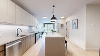 This thoughtfully designed one-bedroom, one-bathroom residence at 1706 Sherman Ave in Evanston, Illinois offers a refined modern aesthetic complemented by warm architectural character. The open-concept kitchen and living area forms the heart of the home, anchored by a large central island with seating — ideal for dining or entertaining. The kitchen features sleek white upper cabinetry, wood-toned lower cabinets, a textured tile backsplash, and stainless steel appliances, all illuminated by striking black pendant lights and recessed ceiling fixtures. Light hardwood flooring runs throughout, enhancing the bright, airy atmosphere. The living area is defined by a large sliding glass door that opens to a private balcony, filling the space with natural light and offering views of the surrounding Evanston neighborhood. A charming exposed brick wall adds warmth and texture to both the living area and bedroom. The bedroom is a calm, well-proportioned retreat featuring recessed lighting and a closet. The bathroom is finished with floor-to-ceiling vertical gray tile, a frameless glass walk-in shower, and matte black fixtures, delivering a clean, spa-like feel. The overall ambiance is contemporary yet inviting, blending modern design elements with classic brick detailing throughout.