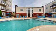 Located at 1601 Cottleville Pkwy in Cottleville, Missouri, this three-floor residential community offers a well-appointed outdoor amenity area designed for both relaxation and social gathering. The centerpiece of the outdoor space is a generously sized freeform swimming pool with clear, blue water, surrounded by an expansive concrete sundeck outfitted with numerous blue lounge chairs and shaded patio seating with umbrellas — ideal for enjoying warm Missouri days.

The pool area is enclosed by a wrought iron fence, providing both security and open sightlines to the surrounding neighborhood. A dedicated spa or wading area is also present, adding to the leisure options available to residents.

Anchoring the amenity area is a two-story clubhouse building, constructed with classic brick and siding exteriors. The building features tall, floor-to-ceiling windows that draw natural light into its interior and serve as an architectural focal point. Multiple entry doors open directly onto the pool deck, facilitating easy indoor-outdoor flow.

Adjacent to the clubhouse, the multi-story residential building rises prominently, with private balconies on each level overlooking the pool and surrounding landscape. Mature evergreen shrubs and landscaping elements add a finishing touch to the outdoor environment, creating an attractive and functional communal space for residents throughout the warmer seasons.