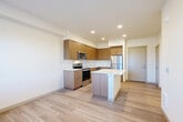 Located at 430 W Stuart Rd in Bellingham, WA, this 2-bedroom, 2-bathroom unit offers a thoughtfully designed single-level layout. The open-concept kitchen and living area serves as the heart of the home, featuring warm wood-toned cabinetry, crisp white quartz countertops, a central kitchen island, and a full suite of stainless steel appliances including a range, microwave, dishwasher, and refrigerator. Light hardwood-style flooring runs throughout the main living area, contributing to a clean, contemporary aesthetic complemented by recessed lighting overhead. The living area receives natural light through a window, creating a bright and inviting atmosphere. Both bedrooms are carpeted and offer a comfortable, quiet retreat, each with windows that bring in natural light. The hallway connects the bedrooms to the two bathrooms and a closet, providing a practical and efficient flow. One bathroom features a full tub-shower combination, while the other includes a wood-toned vanity with a white countertop, undermount sink, and large mirror. The overall design is modern and neutral, with consistent finishes throughout that lend the space a cohesive, move-in-ready feel.