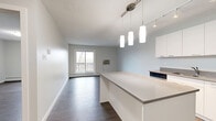 Located at 6703 Rochdale Blvd in Regina, Saskatchewan, this well-designed one-bedroom, one-bathroom unit offers a clean, contemporary aesthetic throughout its thoughtfully laid-out single floor. The open-concept kitchen and living area serves as the heart of the space, featuring a peninsula with a grey quartz-style countertop, crisp white cabinetry, and a full suite of stainless steel appliances including a range, microwave, and dishwasher. Stylish pendant lighting hangs above the peninsula, complementing the track lighting that runs the length of the kitchen. Dark hardwood-style flooring flows seamlessly through the main living area, creating a warm contrast against the light grey walls. A sliding glass door leads to a private balcony, allowing natural light to fill the living room. The bedroom is generously sized, offering a built-in closet with wire shelving, a large window for natural light, and a wall-mounted air conditioning unit. Baseboard heating is present throughout. The bathroom is finished with clean white subway tile surrounding the tub-shower combination, wood-look vinyl flooring, and a white vanity. This unit delivers a modern, functional living space with consistent finishes and a neutral palette throughout.