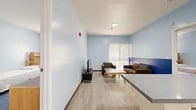 Located at 1091 Everton Pl in Riverside, CA, this single-floor unit offers a thoughtfully arranged layout across nine distinct areas. The interior is finished with light blue walls and white ceilings throughout, creating a clean, consistent aesthetic that promotes a calm and functional atmosphere.

The shared living area features light wood-look flooring, a large window with vertical blinds that invites natural light, and a comfortable seating arrangement centered around a coffee table. A television setup is positioned along one wall, with a blue accent band adding a pop of color to the lower portion of the walls.

The kitchen is well-appointed with white cabinetry, a gas range, microwave, full-size refrigerator, and a deep gray countertop that extends into a peninsula with bar seating — ideal for casual dining or study.

The bedrooms are carpeted in deep blue and include individual wooden dresser units and bed frames, providing each occupant with personal storage. A dedicated walk-in closet area with overhead shelving brackets offers additional organization space.

Two full bathrooms serve the unit, each featuring a tub-shower combo, toilet, vanity with under-sink storage, a gray countertop, and a large mirror. Light wood-look flooring ties these spaces to the rest of the unit. Overall, the space is practical, neatly designed, and well-suited for shared residential living.
