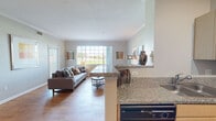 This single-floor residence at 12150 Washington Center Pkwy offers a thoughtfully designed open-concept layout that seamlessly connects the kitchen, dining, and living areas. The living room is bathed in natural light through large grid-pane windows that frame outdoor green views, and features warm hardwood-style flooring and crown molding throughout. The kitchen is outfitted with light maple cabinetry, granite-style countertops, black appliances including a range, refrigerator, and dishwasher, providing ample workspace for everyday cooking. A dedicated dining area accommodates a full-size table and benefits from a stylish pendant light overhead. The bedroom is carpeted for comfort, includes a ceiling fan, a window with outdoor views, and direct access to a spacious walk-in closet equipped with wire shelving systems on multiple walls for organized storage. The bathroom features a wide vanity with light maple cabinetry, a large mirror, and a full tub-shower combination. Consistent hardwood-style flooring flows throughout the main living spaces, while neutral wall tones create a calm, cohesive ambiance across the entire residence.