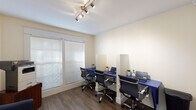 Located at 4711 S Himes Ave in Tampa, Florida, this single-floor professional workspace offers a well-organized and inviting environment designed to support productivity and client comfort. The layout flows from a welcoming entryway — featuring warm wood-look flooring, white paneled French doors with glass panes, and tasteful wall art — into distinct functional areas throughout the space.

The primary workstation room is equipped with a wall-mounted blue desk running the length of the room, divided into individual stations by clear privacy panels. Each station is paired with a modern ergonomic chair, providing a clean and focused environment for multiple users. Track lighting overhead ensures consistent, well-lit conditions, while large windows fitted with horizontal blinds allow natural light to fill the room.

A relaxed reception or waiting area features a plush blue accent chair positioned beneath a large decorative wall clock with a rustic wood face and Roman numerals, adding a warm, stylistic focal point to the space. Lush greenery and a wood-toned storage unit complete the area. Louvered bi-fold closet doors provide additional storage access within the space.

Throughout, the consistent use of wood-look flooring, neutral cream walls, and white trim creates a cohesive, professional aesthetic that is both functional and visually appealing.