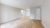 Located at 2460 Fox Harbour Dr S in Indianapolis, Indiana, this single-floor unit presents a clean, updated interior defined by light hardwood-style flooring and neutral warm-gray walls that carry consistently throughout the space. The open floor plan model reveals a generously sized living area that flows toward a sliding glass door fitted with vertical blinds, allowing natural light to enter while providing a view of the surrounding exterior. The living space connects to additional rooms via arched and standard doorways, maintaining an open and accessible layout.

The kitchen features warm wood-toned cabinetry, a countertop peninsula, and a sink, offering functional workspace and storage. Adjacent to the kitchen is a dedicated area equipped with in-unit washer and dryer hookups, including water supply connections and a dryer vent outlet, providing added convenience. A bedroom includes a window with blinds that brings in natural light, a textured ceiling, and access to a walk-in closet with a hanging rod. The full bathroom is finished with light hardwood-style flooring, a white vanity with storage, a toilet, and a tub-shower combination with a chrome fixtures and curtain rod. The overall ambiance is bright, clean, and move-in ready.