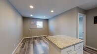 This single-floor space showcases a clean, contemporary design with consistent wood-look luxury vinyl flooring running throughout. The kitchen serves as a central highlight, featuring crisp white shaker-style cabinetry, granite countertops with warm speckled tones, and a full suite of stainless steel appliances including a range, over-the-range microwave, dishwasher, and refrigerator. A white subway tile backsplash adds a polished finishing touch. A peninsula with white cabinetry and a granite countertop extends into the adjacent living area, providing additional workspace or casual seating. Recessed lighting illuminates the open layout effectively, complemented by neutral gray-toned walls that create a cohesive, modern palette throughout. A window-mounted air conditioning unit provides climate control in the main living area. The bathroom is well-appointed with a full tub-shower combination featuring a clean white surround, a white vanity, and matching flooring. A closet with double doors provides practical storage. The space benefits from a private entrance door, adding a sense of independence and convenience to the overall layout.