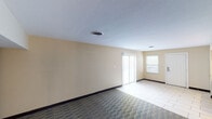 Located at 3553 Founders Rd in Indianapolis, Indiana, this single-floor unit offers a practical and well-appointed layout suited for comfortable living. The open living area is bathed in natural light streaming through a large sliding glass door fitted with vertical blinds, creating a bright and airy atmosphere. The space features a combination of light ceramic tile flooring and patterned geometric carpeting, clearly delineating different functional zones throughout the unit.

The kitchen is a standout feature, showcasing dark espresso cabinetry that extends to the ceiling, complemented by glass-front upper cabinet doors and a decorative tile backsplash in earthy tones. Stainless steel appliances, including a refrigerator, dishwasher, and microwave, lend a modern touch, while the clean white countertops provide ample workspace.

A dedicated area near the kitchen includes a built-in desk with a mirror and light-toned tile flooring, paired with a louvered closet door, adding functional storage to the space. An additional closet with a clothing rod is visible near the entryway, offering practical organization.

The textured ceiling and warm beige walls are consistent throughout, contributing to a cohesive and neutral aesthetic. The unit's straightforward, single-floor design ensures easy accessibility and efficient use of space across all areas.