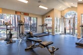Located at 808 Gladstell St in Conroe, Texas, this single-floor fitness center is designed to support a full range of workout routines in a well-equipped, energizing environment. The space features striking vaulted ceilings that lend an open, airy feel, complemented by recessed and panel lighting throughout. Large windows and glass doors line the perimeter, flooding the interior with abundant natural light and offering views of the surrounding outdoor grounds.

The cardio zone is well-appointed with multiple treadmills, elliptical machines, and a stationary bike, all positioned to take advantage of the natural light and outdoor sightlines. A wall-mounted flat-screen TV adds to the motivational atmosphere. The strength training area includes a cable machine, adjustable weight benches, and a full rack of dumbbells, while a dedicated functional training section offers kettlebells, medicine balls in varying weights, and a storage unit for accessories.

Durable rubber flooring covers the workout areas, providing safety and comfort during exercise. Motivational signage is displayed throughout the space, adding character and energy. A ceiling fan and climate control ensure year-round comfort. The overall layout is thoughtfully organized to allow simultaneous use of cardio and strength equipment without congestion, making this fitness center a practical and well-rounded facility.