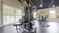 Located at 7200 Gorden Farms Parkway in Dublin, Ohio, this dedicated fitness center offers a well-appointed workout environment designed to support a comprehensive exercise routine. The single-floor space is thoughtfully laid out to accommodate a variety of strength and conditioning equipment without feeling cramped.

The room features a striking dark ceiling that contrasts with the warm cream-toned walls, creating a modern, purposeful aesthetic. Large multi-pane windows along one wall flood the space with abundant natural light and provide views of the surrounding greenery, contributing to an energizing atmosphere for workouts.

The fitness center is equipped with a robust multi-station cable machine that supports a wide range of resistance training exercises, along with adjustable benches and a power rack suitable for free weight training. Durable rubber flooring covers the workout area, providing both safety and practicality. Overhead pendant and recessed lighting supplements the natural light, ensuring the space is well-illuminated at all times.

A wall-mounted mirror enhances the sense of space and allows users to monitor their form during exercise. The overall layout is clean and organized, making efficient use of the available floor area. This fitness center provides a functional and inviting environment well-suited for residents seeking convenient, on-site access to quality exercise facilities.
