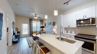 This well-designed single-floor residence offers a seamless open-concept layout that connects the kitchen, dining, and living areas into one cohesive and functional space. The kitchen is a standout feature, showcasing crisp white shaker cabinetry, quartz countertops, a subway tile backsplash, stainless steel appliances including a refrigerator, range, and microwave, and a generous island with bar seating — ideal for casual dining and entertaining. Track and pendant lighting accentuate the clean, modern aesthetic throughout the kitchen.

The living area is bright and welcoming, filled with natural light from large windows dressed with plaid curtains and a sliding glass door providing outdoor access. Wood-look flooring runs throughout the main living spaces, while a ceiling fan adds comfort overhead.

Two bedrooms offer comfortable retreats, each featuring plush carpeting, generous windows with sheer curtains, and ceiling fans. The primary bedroom connects directly to an en-suite bathroom appointed with dual white vanities, quartz countertops, large mirrors, and direct access to a spacious walk-in closet with built-in shelving.

The overall ambiance is contemporary and inviting, with a neutral color palette, modern fixtures, and thoughtful design details that make this space both functional and visually appealing.
