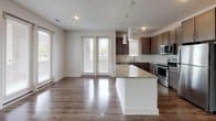 Located at 800 Finsbury St in Durham, NC, this well-appointed single-floor residence offers a thoughtfully designed layout with modern finishes throughout. The open-concept living and dining area is anchored by rich wood-look hardwood flooring, a ceiling fan, and generous windows fitted with blinds that invite ample natural light while maintaining privacy.

The kitchen is a standout feature, showcasing dark taupe shaker-style cabinetry, granite countertops, a subway tile backsplash, and a large central island with pendant lighting overhead. A full suite of stainless steel appliances — including a range, over-the-range microwave, refrigerator, and dishwasher — completes this functional and attractive space, which opens seamlessly toward the living area and a glass-panel exterior door.

The bedrooms are carpeted for comfort, each offering neutral tones, windows with outdoor views, and ample wall space. Two bathrooms serve the residence: one features a granite-topped vanity with gray cabinetry and a combination tub/shower, while the other offers a walk-in glass-enclosed shower, matching vanity, and wood-look flooring. Both bathrooms maintain a clean, contemporary aesthetic consistent with the rest of the home's design.