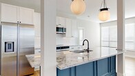 Located at 1140 Chambers Rd in Columbus, Ohio, this thoughtfully designed 2-bedroom, 2-bathroom residence offers a refined living experience across a single, well-appointed floor. The open-concept kitchen and living area serves as the heart of the home, showcasing a striking blue kitchen island topped with elegant granite countertops, white shaker cabinetry, a decorative arabesque tile backsplash, and stainless steel appliances. Globe pendant lights add a sophisticated finishing touch overhead, while light hardwood flooring flows throughout the main living areas, enhancing the bright, airy atmosphere. The primary bedroom is generously sized, featuring plush carpet, multiple windows for ample natural light, and an accent wall adorned with classic raised panel molding. It connects to a well-appointed bathroom complete with marble-look tile flooring, a glass-enclosed shower, and built-in shelving. The second bedroom also benefits from hardwood flooring and large windows. Two closets provide practical storage solutions, with built-in shelving and hanging rods. Crisp white panel doors with matte black hardware carry a consistent modern aesthetic throughout the hallways and rooms, tying together a clean, contemporary design sensibility.