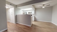 This single-floor residence offers a thoughtfully designed open-concept layout that connects the kitchen and living areas seamlessly. The kitchen is equipped with white shaker-style cabinetry, stainless steel appliances including a refrigerator and range, a under-cabinet range hood, and light-toned countertops. A peninsula with a gray finish provides additional workspace and casual seating. A skylight positioned above the kitchen fills the space with natural light, complementing the light wood-look flooring that extends throughout the main living areas.

The living room is generously proportioned, featuring a ceiling fan with integrated lighting, neutral gray walls, and a sliding glass door fitted with vertical blinds that allows natural light to pour in and provides access to an outdoor area. The bedrooms are carpeted for added comfort, with neutral two-tone wall treatments. One bedroom features a sliding double-door closet and a window with a horizontal blind. Another bedroom offers access to an adjoining room or hallway through a barn-style door. The bathroom is finished with a white vanity, gray countertop, a large mirror, matte black fixtures, and a tiled tub and shower combination, all set on wood-look flooring for a cohesive, contemporary feel throughout.