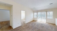 Located at 982 Summitville Dr in Webster, NY, this single-floor residence offers a well-organized and functional layout filled with natural light throughout. The open living area is highlighted by vaulted ceilings, warm beige carpeting, and a sliding glass patio door flanked by vertical blinds, allowing generous sunlight to pour in. A half-wall partition adds a subtle architectural detail that defines the space without closing it off. An adjoining room, accessible through a doorway from the living area, provides additional flexible living space, also finished with plush carpeting and a window with outdoor views. The kitchen is efficiently designed with light wood cabinetry, ample counter space, tile flooring, and a full suite of appliances including an electric range, over-the-range microwave, and refrigerator. A double-basin sink sits beneath a window, and a breakfast bar-style counter connects the kitchen to the living space. The residence includes two bathrooms: a full bath featuring a tub/shower combination with chrome fixtures and a wood-toned vanity, and a half bath with a single-sink vanity and mirror. Additional bedrooms feature carpeted floors, neutral walls, and windows that bring in natural light. Textured ceilings are present throughout the home, contributing to a cohesive interior aesthetic.