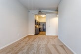 Located at 315 Delaware St in Kansas City, MO, this single-floor unit blends industrial character with modern finishes throughout its thoughtfully arranged layout. Exposed ductwork and pendant lighting run across the elevated ceilings in the main living area, lending an urban loft aesthetic to the space. Soft, neutral carpet covers the generously sized living and bedroom areas, while tall windows allow natural light to filter in and contribute to an open, airy feel. A ceiling fan in the bedroom adds both function and comfort.

The kitchen is outfitted with sleek, dark cabinetry paired with gray countertops and a full suite of black appliances, including a range, microwave, dishwasher, and refrigerator. Light wood-tone flooring runs throughout the kitchen, providing a warm contrast to the darker cabinetry. The layout offers ample counter and storage space along a galley-style configuration.

The bathroom continues the unit's consistent design language with a dark vanity cabinet, gray countertop, undermount sink, and a large mirror with wall-mounted lighting fixtures above. Wood-tone flooring grounds the space. Overall, the unit presents a cohesive industrial-modern aesthetic well-suited to urban living in Kansas City.