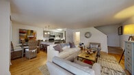 This two-floor residence is thoughtfully designed with a comfortable, contemporary aesthetic and a seamless flow between living spaces. The main level centers around an open-concept layout where the living room, dining area, and kitchen connect naturally. The living room features light hardwood flooring, a patterned area rug, and generous seating, creating a welcoming gathering space. A staircase leads to the upper floor, adding to the home's multi-level character.

The kitchen is well-equipped with sage-toned shaker-style cabinetry, dark granite countertops, stainless steel appliances, and pendant lighting over a central island that doubles as a breakfast bar. The space is both functional and stylish, ideal for everyday cooking and entertaining alike.

The upper level hosts the bedrooms, each finished with neutral carpet and bright white walls. The primary bedroom is a standout, featuring a dramatic dark wood four-poster canopy bed, natural light from a woven shade window, and a spacious closet. A second bedroom accommodates twin beds with charming blue-painted headboards and a window with a bamboo shade. A full bathroom with tile flooring, a tub/shower combination, and a white vanity completes the upper level with clean, classic finishes.