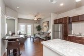 This single-floor residence offers a thoughtfully designed layout that balances comfort and functionality throughout. The kitchen is a standout feature, equipped with stainless steel appliances including a refrigerator, range, microwave, and dishwasher. Rich, dark espresso cabinetry reaches toward the ceiling, complemented by light granite countertops, a classic subway tile backsplash, hardwood-style flooring, and a peninsula island that provides additional prep and dining space. Pendant lighting adds a refined touch overhead.

The living area flows naturally from the kitchen and is finished with the same warm hardwood-style flooring. A ceiling fan overhead and large French doors leading to an outdoor area fill the space with natural light and provide a seamless indoor-outdoor connection. The entry foyer features a full-size front door and is accented by bold artwork and a decorative indoor plant.

Both bedrooms are carpeted and outfitted with ceiling fans. One bedroom includes a window with outdoor views and a rich wood dresser with mirror, while the other connects to an adjacent room via a glass-panel door. The bathroom is accessed through a hallway and features a dark wood vanity, granite countertop, and a large mirror, continuing the cohesive, modern aesthetic found throughout the residence.