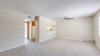 This efficiently designed single-story unit offers a thoughtful layout across a compact footprint. The combined living room and kitchen area serves as the heart of the space, featuring plush wall-to-wall carpeting, neutral beige walls, a textured ceiling, and a ceiling fan with integrated lighting. A pass-through window connects the living area to the kitchen, enhancing the sense of openness between the two spaces. The kitchen is configured in a galley style, equipped with warm wood cabinetry, granite-patterned countertops, a mosaic tile backsplash, white appliances, and wood-look vinyl flooring that adds visual warmth and easy maintenance.

The bedroom is a generously proportioned room featuring soft carpeting, a ceiling fan, and a sliding glass door that opens to a private balcony overlooking lush greenery. A secondary window also provides natural light. The room is accessible via a hallway that connects to a dedicated closet for storage.

The bathroom is clean and functional, featuring a full tub-shower combination with white subway tile surround, chrome fixtures, and wood-look flooring. A hallway with hardwood-style flooring links all areas of the unit, providing clear circulation throughout the space.