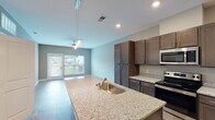 Located at 921 Trailwood Dr in Raleigh, NC, this single-floor residence offers a thoughtfully designed layout with modern finishes throughout. The kitchen serves as a central highlight, featuring rich dark-toned cabinetry, light granite countertops, and a full suite of stainless steel appliances including a refrigerator, electric range, and over-the-range microwave. A large center island with a granite surface and built-in sink provides additional prep space and serves as a natural gathering point. Light wood-style flooring runs throughout the main living and kitchen areas, lending warmth and continuity to the open floor plan. Recessed lighting illuminates the space cleanly from above. A dedicated laundry area is conveniently accessible just off the kitchen. The bathroom is finished with light wood-look flooring, neutral taupe walls, chrome hardware, and a full tub-shower combination. Bedrooms feature plush wall-to-wall carpeting and are filled with natural light through double windows fitted with white blinds, offering pleasant outdoor views of surrounding greenery. The overall aesthetic is clean, neutral, and move-in ready, reflecting a well-maintained and functional living environment.