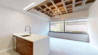 This thoughtfully designed single-floor space masterfully combines industrial character with modern finishes. The open living and kitchen area serves as the heart of the unit, immediately drawing the eye to a striking exposed waffle-slab concrete ceiling — a bold architectural detail that adds raw texture and depth. A mid-century-inspired sputnik chandelier hangs beneath it, complementing the industrial aesthetic with a stylish accent. Linear recessed lighting and track lighting further enhance the ambiance.

Floor-to-ceiling windows span the living area, flooding the space with natural light and offering views of the surrounding urban greenery. The open kitchen features warm wood cabinetry with brushed metal hardware, a crisp white countertop island with a deep stainless steel sink and professional-style faucet, stainless steel appliances, and a vibrant teal mosaic tile backsplash that adds a pop of color.

The bathroom continues the design cohesion with a walk-in shower adorned with teal subway tiles, a white quartz vanity, and warm wood cabinetry. A dedicated bedroom area includes a spacious reach-in closet with built-in shelving and hanging rods. Throughout, light neutral flooring ties the spaces together, creating a clean, cohesive, and inviting atmosphere.