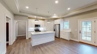 Located at 5833 Evans Farm Dr. in Lewis Center, Ohio, this single-floor home offers a thoughtfully designed open-concept layout with modern finishes throughout. The entryway leads down a clean, well-lit hallway with recessed lighting and durable hardwood-style flooring, providing a welcoming introduction to the home.

The kitchen is a standout feature, showcasing white shaker-style cabinetry, stainless steel appliances including a range, microwave, and refrigerator, and a large center island with a double sink and light countertops. Dual industrial-style pendant lights hang above the island, adding a contemporary touch. The kitchen flows seamlessly into the open living area, which is defined by an elegant tray ceiling, recessed lighting, a ceiling fan, and French doors that allow natural light to pour in while providing views of the outdoors.

A full bathroom features a tub-shower combination with white tile surround, a white vanity, and wood-look flooring. The home also includes a dedicated laundry area equipped with a full-size washer and dryer, as well as a walk-in closet with wire shelving for generous storage. The attached two-car garage offers additional utility space with an automatic opener. Neutral tones and clean architectural lines create a cohesive, move-in-ready atmosphere throughout.