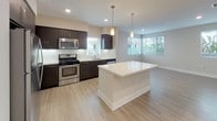 This thoughtfully designed single-floor unit blends modern aesthetics with functional living. The entry foyer welcomes you with light wood-tone flooring and clean neutral walls, providing a seamless transition into the open-concept main living area. The kitchen is a standout feature, boasting rich dark espresso cabinetry, crisp white quartz countertops, stainless steel appliances including a gas range, microwave, refrigerator, and dishwasher, along with a deep single-basin sink. A central island with pendant lighting above serves as both a prep space and casual gathering point, flowing naturally into the bright, airy living area bathed in natural light from multiple windows dressed with horizontal blinds. An exterior door in the living space provides convenient outdoor access. The two bedrooms are generously sized, each featuring plush wall-to-wall carpeting and sizable windows that frame views of surrounding greenery, filling the rooms with natural light. Both bathrooms are finished in a clean, contemporary style with light wood-look tile flooring, white soaking tub-shower combinations, and well-appointed vanities. The overall ambiance of the unit is calm and modern, with a consistent palette of warm neutrals and quality finishes that create a cohesive, move-in-ready living environment.