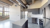 This 2-bedroom, 2-bathroom unit in Memphis, TN offers a compelling blend of industrial character and contemporary design. Soaring ceilings with exposed ductwork, structural beams, and warehouse-style pendant lighting set a distinctive urban tone throughout the open living spaces. Polished concrete floors run seamlessly across the entire unit, reinforcing the loft-inspired aesthetic.

The kitchen is a standout feature, outfitted with sleek gray cabinetry, a white subway tile backsplash, granite countertops, and a generously sized island ideal for meal prep or casual dining. Stainless steel appliances, including a range, microwave, dishwasher, and refrigerator, complete the well-appointed space.

The living area benefits from an impressive wall of large industrial-style windows framed by exposed brick, allowing abundant natural light and offering views of the surrounding greenery. The open layout provides a flexible, spacious feel.

Both bathrooms echo the unit's modern design language, featuring gray vanities with granite countertops and polished chrome fixtures. One bathroom includes a full tub-shower combo with white subway tile surround, while the second offers a clean, functional layout. The overall ambiance is sleek, modern, and effortlessly urban, making this unit a distinctive residence in the Memphis market.