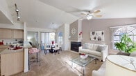 This single-floor residence is thoughtfully designed with an open-concept layout that seamlessly connects the living, dining, and kitchen areas. The living room is a standout space, featuring soaring vaulted ceilings, a ceiling fan with light fixture, and a tiled fireplace with a white surround that serves as the room's focal point. Soft, neutral-toned carpeting runs throughout the main living areas and bedrooms, creating a warm and cohesive atmosphere. The dining area is bathed in natural light courtesy of a large sliding glass door and an arched window, complemented by a pendant light overhead.

The kitchen is well-appointed with light wood cabinetry, granite-style countertops, stainless steel appliances including a refrigerator, range, and microwave, and an extended breakfast bar that opens to the main living space. Light wood-look flooring adds a clean, functional touch to the kitchen.

The primary bedroom offers vaulted ceilings, a generous window with outdoor views, and direct sightlines to the living area. A second bedroom features a large sliding-door closet with built-in shelving, providing excellent storage. The bathroom is notably spacious, with a long dual-sink vanity, ample counter space, and light tile flooring, offering a clean and functional design throughout.
