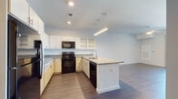 This single-floor unit offers a well-designed open-concept layout with modern finishes throughout. The kitchen serves as a central feature, equipped with granite countertops, a large peninsula with an integrated sink, white upper cabinetry with open shelving, and a full suite of black appliances including a refrigerator, range, microwave, and dishwasher. Wood-style flooring runs through the kitchen and main living areas, complementing the bright, neutral color palette.

The living area is spacious and airy, featuring a ceiling fan and sliding glass door that opens to a private balcony, providing natural light and outdoor views of the surrounding neighborhood. A second bedroom offers plush carpeting, a ceiling fan, and a large window with additional natural light, along with access to an outdoor area.

The primary bedroom includes soft carpeting, a walk-in closet, and an en-suite bathroom finished with granite countertops, white cabinetry with gold hardware, a wall-mounted mirror with vanity lighting, and large-format tile flooring. A separate half bathroom features a wall-mounted sink, a tall mirror, and matching tile flooring. A dedicated laundry room with a full-size washer and dryer completes the unit.