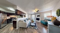 This thoughtfully designed 1-bedroom, 1-bathroom residence offers a functional and stylish open-concept floor plan across a single level. The combined living, dining, and kitchen area forms the heart of the home, anchored by rich wood-style flooring and a textured ceiling with a ceiling fan. The living room is bright and welcoming, featuring a white brick fireplace, large windows, and sliding glass doors that invite natural light and provide access to an outdoor area. A half-wall peninsula seamlessly separates the kitchen from the living space, maintaining an open and airy feel. The kitchen is well-equipped with dark espresso cabinetry, a mosaic tile backsplash, stainless steel appliances including a range, dishwasher, and refrigerator, and generous counter space. A cozy dining nook accommodates a bistro-style high-top table, perfect for casual meals. The spacious primary bedroom features plush carpeting, a ceiling fan, a large window for natural light, and a walk-in closet. The full bathroom includes a vanity with dark cabinetry, a tub-shower combination, and wood-style flooring, completing this efficient and comfortable layout.