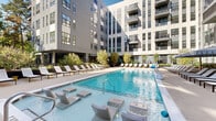 Located at 600 St Albans Dr in Raleigh, North Carolina, this contemporary residential community showcases a striking multi-story architectural design characterized by a neutral palette of gray paneling, bold black-framed windows, and private balconies that overlook a beautifully appointed central courtyard.

At the heart of the community lies a resort-style pool deck, the defining feature of the outdoor amenity space. The generously sized swimming pool is surrounded by an expansive sun deck outfitted with rows of modern lounge chairs and chaise lounges, including in-water seating platforms for ultimate relaxation. Striped umbrellas provide shaded retreats, while manicured planters filled with trees and native greenery create a lush, park-like atmosphere throughout.

A dedicated outdoor recreation area complements the pool deck, featuring a shuffleboard table set on artificial turf beneath a covered terrace. Floor-to-ceiling glass walls and mature tree canopies frame this space, connecting it visually to the surrounding natural environment.

Thoughtfully designed pedestrian pathways and landscaped entry corridors with curated planters, young trees, and clean-lined benches tie the outdoor spaces together. The overall ambiance strikes a balance between urban sophistication and relaxed, resort-style living, making this courtyard amenity space a standout feature of the Raleigh community.