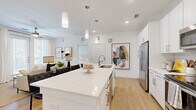 This well-designed 2-bedroom, 2-bathroom single-floor residence offers a thoughtfully planned open-concept layout finished with light wood-style flooring and a clean, contemporary aesthetic throughout. The kitchen serves as the heart of the home, showcasing crisp white cabinetry, a large quartz waterfall island with bar seating, stainless steel appliances, a tile backsplash, and elegant pendant lighting — all flowing seamlessly into the adjacent living and dining areas. The living room is bright and inviting, featuring a ceiling fan, sheer floor-to-ceiling curtains, and a glass door that floods the space with natural light. The primary bedroom provides a comfortable retreat, complete with its own closet and easy access to a full bathroom featuring a tub-shower combo with tile surround, white vanity cabinetry, and wood-look flooring. A second bedroom and additional full bathroom offer flexibility for guests or roommates. Two dedicated closets — including a walk-in with wire shelving systems — provide generous storage throughout. The residence maintains a consistent modern palette of white walls and light flooring, creating a cohesive, bright, and welcoming atmosphere from room to room.