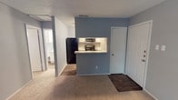 This single-story unit at 2101 Park Springs Blvd in Arlington, Texas presents a practical and cohesive layout finished in soft gray tones throughout. The living area features plush carpeting and opens directly toward the kitchen via a pass-through counter with a light-toned quartz-style surface, creating a connected feel between the two spaces. A dark hardwood-style floor transitions at the entryway, providing a durable surface near the front door.

The kitchen is efficiently arranged in a galley configuration, featuring white cabinetry with brushed nickel hardware, quartz-style countertops with a subtle speckled pattern, a stainless steel sink, a black electric range, stainless steel microwave, and a tile backsplash. A louvered-door closet at the end of the kitchen provides additional storage.

The bedroom is generously sized with soft carpeting, a ceiling fan with light fixture, a window allowing natural light and outdoor views, and access to a closet. The bathroom is well-appointed with wood-style flooring, a single-sink vanity with quartz-style countertop, white cabinetry, a framed mirror with lighted bar fixture, and a full tub-shower combination. Textured ceilings are present throughout the unit.