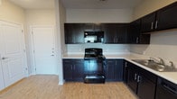 This single-story, one-bedroom, one-bathroom residence offers a practical and well-designed layout that maximizes its compact footprint. The open-concept living and kitchen area creates a seamless flow, with light wood-style flooring extending throughout the main spaces. The kitchen is a standout feature, outfitted with dark espresso cabinetry offering ample upper and lower storage, light-colored countertops, and a full suite of black appliances including an electric range, over-the-range microwave, dishwasher, and refrigerator. A sink with a double basin completes the functional workspace.

The living area is bright and airy, benefiting from a large window that allows natural light to fill the room, complemented by a ceiling fan overhead. Neutral-toned walls and clean white baseboards contribute to a simple, cohesive aesthetic throughout.

The bedroom continues the light and neutral palette, featuring plush carpeting, a ceiling fan, and a window providing natural light and outside views. The full bathroom is finished with light tile flooring, a tub/shower combination, and a vanity with dark cabinetry that coordinates with the kitchen finishes, maintaining a consistent design language across the unit.