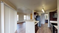 This 1-bedroom, 1-bathroom unit is thoughtfully laid out across a single floor, offering a comfortable and functional living experience. The open-concept design connects the kitchen and living area seamlessly, creating a bright and airy atmosphere enhanced by multiple windows that invite abundant natural light.

The kitchen is a standout feature, equipped with dark espresso cabinetry, stainless steel appliances — including a refrigerator, microwave, and dishwasher — and light-toned countertops. A kitchen island with a built-in sink adds both workspace and a casual dining option. Wood-look flooring runs throughout the kitchen and main living areas, contributing to a warm, cohesive aesthetic.

The living room is generously proportioned, featuring large windows and a sliding glass door that further brighten the space and provide access to the outdoors. The bedroom is carpeted for comfort, fitted with a ceiling fan, and includes a window with an outdoor view, creating a calm and restful retreat.

The bathroom is well-appointed with a dual-sink vanity topped with white countertops, dark cabinetry with brushed nickel hardware, a large mirror with overhead lighting, and a tiled bathtub and shower combination. Wood-look flooring continues into the bathroom, tying the overall design together with consistency and style.