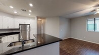 This single-floor residence offers a thoughtfully designed layout that balances functional living spaces with modern finishes. The kitchen serves as a central highlight, showcasing crisp white shaker-style cabinetry, dark granite countertops, and a full suite of stainless steel appliances including a refrigerator, range, microwave, and dishwasher. A peninsula with an integrated sink adds additional prep space and creates a natural divide between the kitchen and the adjoining living area. Wood-look flooring runs through the kitchen and main living areas, contributing warmth and continuity throughout. The living space is open and versatile, with neutral gray walls that complement the overall palette. Multiple bedrooms are finished with plush carpeting, ceiling fans, and window coverings, providing comfort and privacy. Several bedrooms feature sliding glass doors that open to exterior views, allowing natural light to fill the rooms. The bathrooms are clean and functional — one features a full tub-shower combination, a white vanity with a single sink, a large mirror, and wood-look flooring, while a separate water closet provides additional convenience. Recessed lighting throughout the main areas and a neutral color scheme give the space a bright, move-in-ready feel.