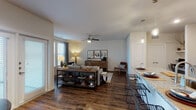 This single-floor residence offers a thoughtfully designed open-concept layout that seamlessly connects the living, dining, and kitchen areas. Rich dark hardwood-style flooring runs throughout the main living spaces, anchoring a warm and inviting atmosphere complemented by neutral walls and abundant natural light from multiple windows with blinds and draping curtains.

The kitchen is a standout feature, showcasing white shaker-style cabinetry reaching to the ceiling, granite countertops, stainless steel appliances including a refrigerator with ice maker, electric range, and microwave. A large granite-topped island with an undermount sink doubles as a breakfast bar with stylish metal bar seating, illuminated by contemporary pendant lighting overhead.

The open living area provides generous space for comfortable furnishings and is finished with a ceiling fan. Windows along one wall invite natural light and outdoor views, creating a bright and airy setting.

The primary bedroom features plush carpeting, a ceiling fan, and a trio of windows that bring in ample natural light. It connects to a well-appointed bathroom with dual undermount sinks, granite countertops, taupe shaker cabinets, and wood-look flooring. An adjacent walk-in closet offers extensive built-in shelving for organized storage. A second bedroom, also carpeted and ceiling fan-equipped, includes a standard closet and offers a calm, restful retreat.