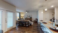 This single-floor residence offers a thoughtfully designed open-concept layout that seamlessly connects the living, dining, and kitchen areas. Rich dark hardwood-style flooring runs throughout the main living spaces, anchoring a warm and inviting atmosphere complemented by neutral walls and abundant natural light from multiple windows with blinds and draping curtains.

The kitchen is a standout feature, showcasing white shaker-style cabinetry reaching to the ceiling, granite countertops, stainless steel appliances including a refrigerator with ice maker, electric range, and microwave. A large granite-topped island with an undermount sink doubles as a breakfast bar with stylish metal bar seating, illuminated by contemporary pendant lighting overhead.

The open living area provides generous space for comfortable furnishings and is finished with a ceiling fan. Windows along one wall invite natural light and outdoor views, creating a bright and airy setting.

The primary bedroom features plush carpeting, a ceiling fan, and a trio of windows that bring in ample natural light. It connects to a well-appointed bathroom with dual undermount sinks, granite countertops, taupe shaker cabinets, and wood-look flooring. An adjacent walk-in closet offers extensive built-in shelving for organized storage. A second bedroom, also carpeted and ceiling fan-equipped, includes a standard closet and offers a calm, restful retreat.