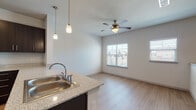 Located at 950 FM-2001 in Buda, Texas, this single-story residence offers a thoughtfully designed layout that balances comfort and functionality. The open-concept kitchen is a standout feature, showcasing rich dark cabinetry, granite-style countertops, a peninsula with a double stainless steel sink, and pendant lighting that adds a warm, modern touch. Stainless steel appliances — including a refrigerator, range, and microwave — complete the kitchen's polished look. Light wood-style flooring flows through the kitchen and living areas, creating a cohesive and inviting atmosphere. The living area benefits from natural light through multiple windows fitted with blinds, and a ceiling fan ensures year-round comfort. The bedrooms are generously sized, each featuring plush carpeting, ceiling fans with lighting, and ample natural light from windows. The walk-in closet offers built-in shelving and a window, providing both storage capacity and brightness. The bathroom is clean and functional, featuring a full soaking tub with tiled surround, wood-style flooring, and dark cabinetry for storage. The overall design is clean, contemporary, and move-in ready, making this Buda residence a practical and comfortable home.