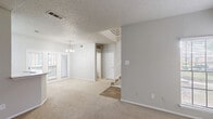 Located at 6000 Ohio Dr in Plano, TX, this two-story home offers a practical and well-organized layout across two floors. The main level features an open-concept kitchen and living area with soft carpet throughout the living space and durable wood-look flooring in the kitchen. The kitchen is equipped with white cabinetry, a peninsula with light stone countertops, a full suite of white appliances including a refrigerator, electric range, built-in microwave, and a double-basin sink. A chandelier-lit dining area sits adjacent, bathed in natural light from French doors that open to the exterior. The living room extends comfortably, with additional windows providing ample brightness. A staircase with white railings connects the floors, and a convenient half bath and laundry area round out the main level. Upstairs, three carpeted bedrooms offer comfortable retreats, each with windows that let in natural light. The primary bedroom includes a walk-in closet with built-in shelving rods for generous storage. Two additional bathrooms serve the upper level, each featuring tub/shower combinations and light stone vanity countertops. Textured ceilings and neutral gray walls are consistent throughout, lending the home a clean, cohesive aesthetic.