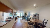 This single-floor residence offers a well-organized layout that balances open communal spaces with private retreats. The living area is generously proportioned, featuring wood-look flooring, a textured ceiling, and a fireplace that anchors the room. Natural light filters in through windows dressed with teal curtains, complementing the neutral wall tones. The space flows seamlessly into a dedicated dining area, which accommodates a round stone-top table and is accented by a metal open-shelf display unit.

The kitchen is equipped with warm honey-toned wood cabinetry, granite-look countertops, and black appliances including a range, over-the-range microwave, and refrigerator. Wood-look flooring continues here, maintaining visual continuity throughout the common areas.

Two bedrooms provide comfortable accommodations. The primary bedroom features soft carpeting, a ceiling fan with integrated lighting, and room for a full furniture arrangement. The secondary bedroom also includes carpet flooring, a walk-in closet, and a window offering natural light.

Both bathrooms are fitted with full tub-shower units featuring built-in shelving niches and chrome fixtures, presenting clean, functional designs. Overall, the space offers a cohesive, comfortable environment with consistent finishes throughout.