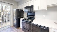 Located at 9201 Rainbow Springs Ct in Louisville, Kentucky, this single-floor unit offers a well-organized layout with a neutral color palette of soft gray tones throughout. The living areas are finished with plush wall-to-wall carpeting and feature white trim and blinds that allow natural light to filter in through multiple windows, creating a bright and welcoming atmosphere. The kitchen is equipped with white shaker-style cabinetry, light quartz countertops, and a full suite of black appliances including a refrigerator, electric range, over-the-range microwave, and dishwasher, all set atop durable wood-look flooring. The bedrooms are generously sized, each with carpet flooring, ample natural light from oversized windows, and ceiling fans for year-round comfort. The bathroom features a clean, white tub-shower combination with tile surround and chrome fixtures. A hallway with wood-look flooring connects the main rooms, with closet storage visible from the corridor. The unit also includes access to a private balcony enclosed by a dark metal railing, offering pleasant views of mature trees and the surrounding community. The overall ambiance is clean, neutral, and move-in ready.